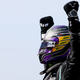 A photo of Lewis Hamilton in black racing overalls with his arms in the air.